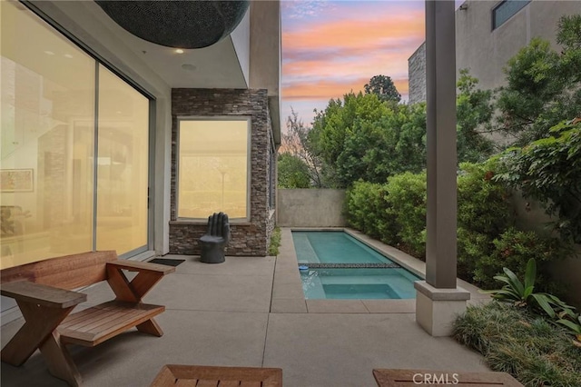 pool at dusk featuring an in ground hot tub and a patio