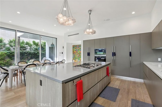 kitchen featuring decorative light fixtures, light hardwood / wood-style floors, stainless steel gas cooktop, and a spacious island