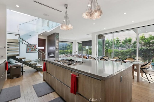 kitchen featuring decorative light fixtures, a notable chandelier, stainless steel gas stovetop, a large island, and light hardwood / wood-style floors