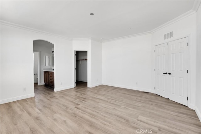 unfurnished bedroom featuring ensuite bathroom, ornamental molding, and light wood-type flooring