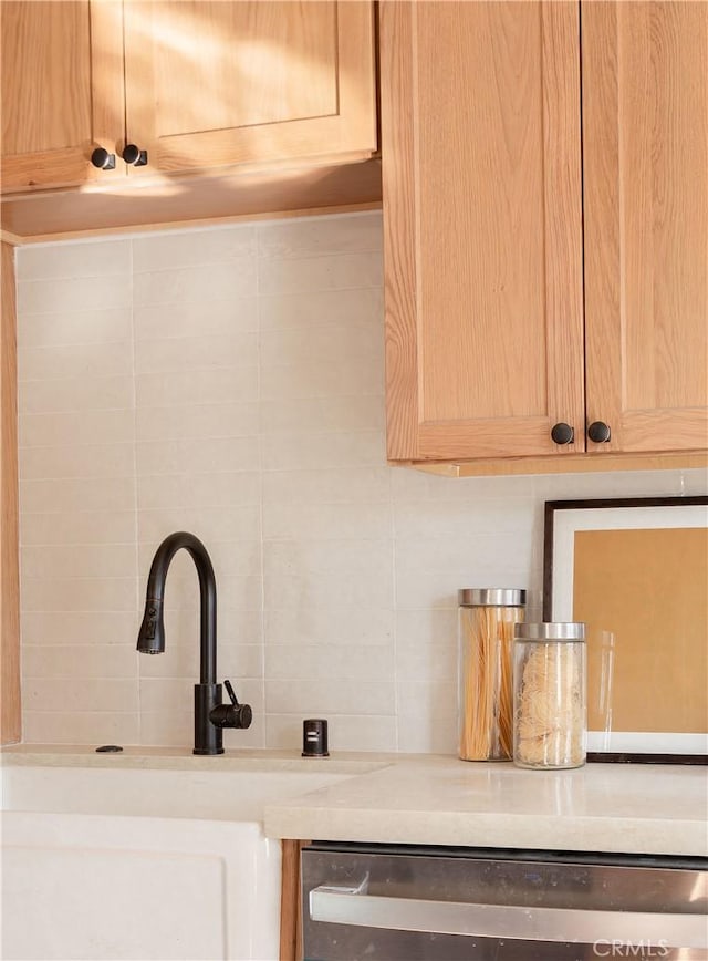 interior details with stainless steel dishwasher, light brown cabinets, sink, and tasteful backsplash