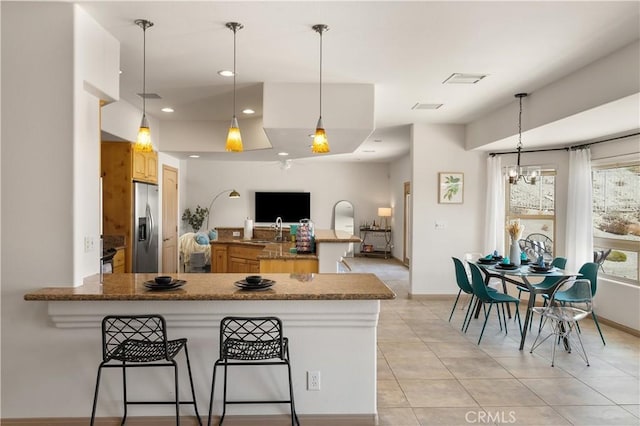 kitchen with kitchen peninsula, stainless steel refrigerator with ice dispenser, a kitchen bar, pendant lighting, and an inviting chandelier