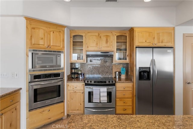 kitchen featuring decorative backsplash, appliances with stainless steel finishes, light brown cabinetry, light stone counters, and exhaust hood