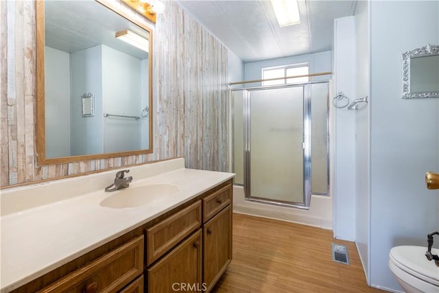 bathroom featuring vanity, wood walls, wood-type flooring, toilet, and a shower with shower door