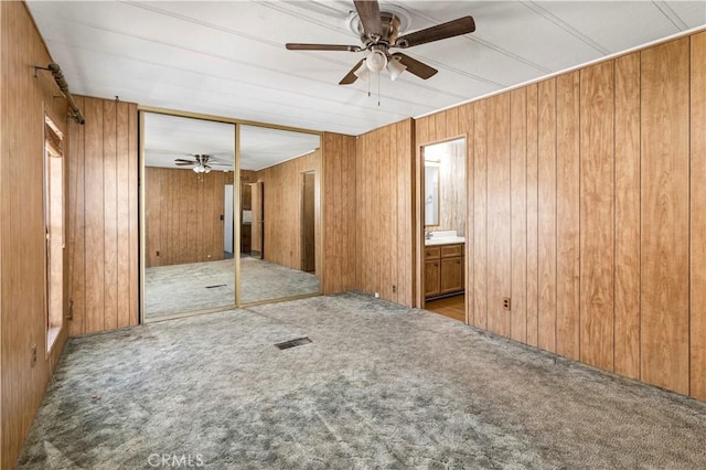 carpeted empty room with ceiling fan and wooden walls