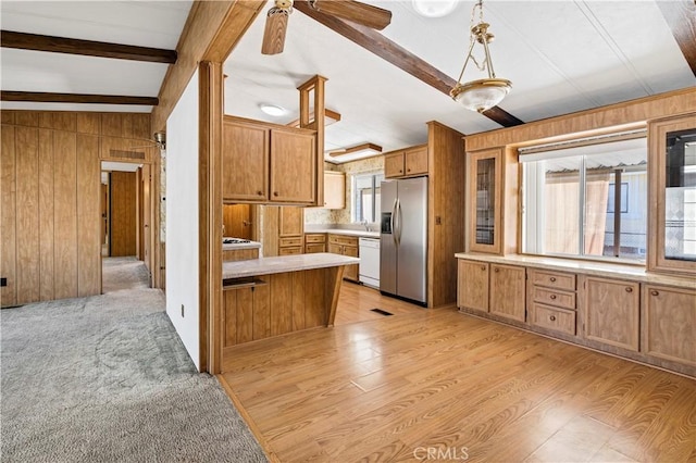 kitchen featuring wood walls, white dishwasher, vaulted ceiling with beams, light wood-type flooring, and stainless steel fridge with ice dispenser