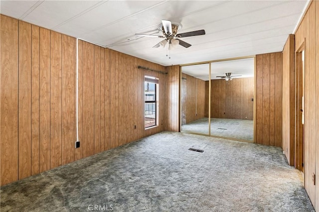 unfurnished bedroom with ceiling fan, wood walls, carpet floors, and a closet