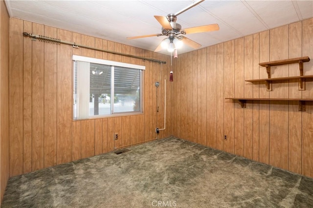 unfurnished room with carpet flooring, ceiling fan, and wooden walls