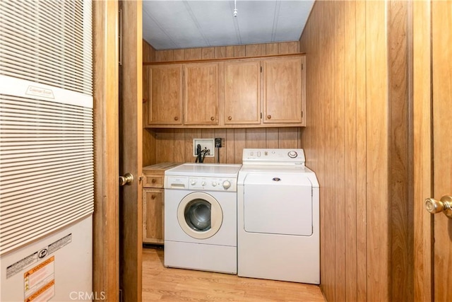 laundry area with cabinets, light hardwood / wood-style flooring, wooden walls, and washing machine and clothes dryer