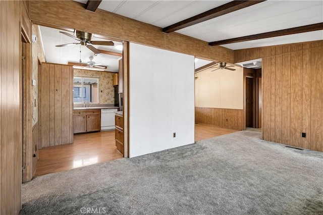 unfurnished living room with beam ceiling, sink, light hardwood / wood-style floors, and wood walls