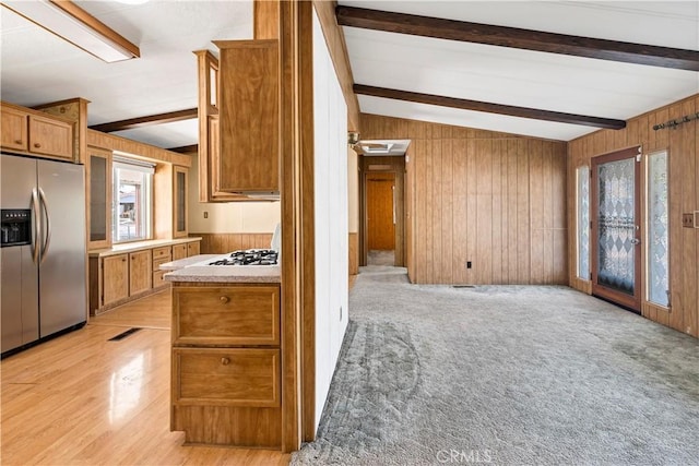 kitchen with stainless steel refrigerator with ice dispenser, light wood-type flooring, white gas cooktop, wooden walls, and lofted ceiling with beams