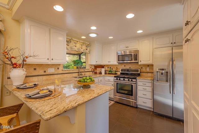 kitchen featuring sink, a breakfast bar area, light stone counters, white cabinetry, and stainless steel appliances