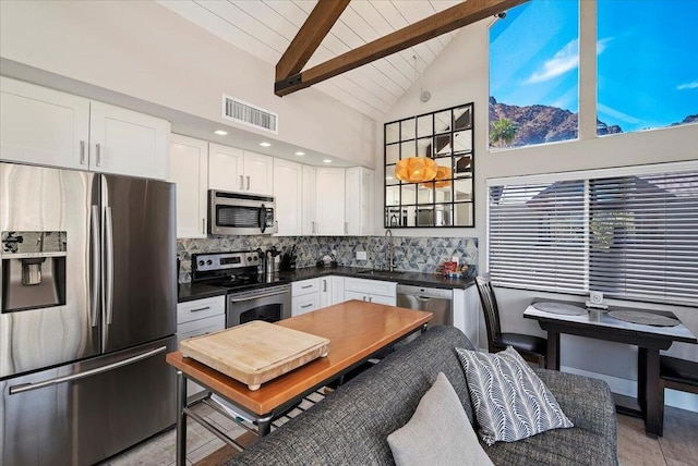 kitchen featuring appliances with stainless steel finishes, white cabinetry, beamed ceiling, decorative backsplash, and high vaulted ceiling