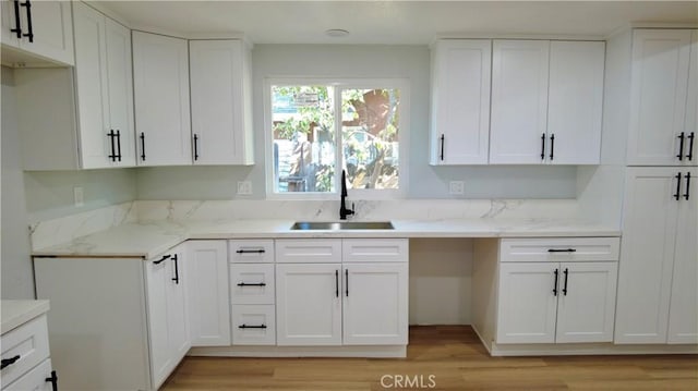 kitchen with white cabinets, light wood-type flooring, light stone countertops, and sink