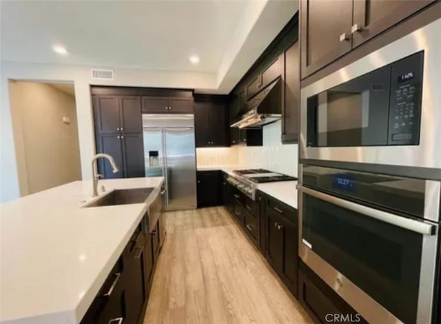 kitchen featuring built in appliances, dark brown cabinetry, sink, and light hardwood / wood-style floors