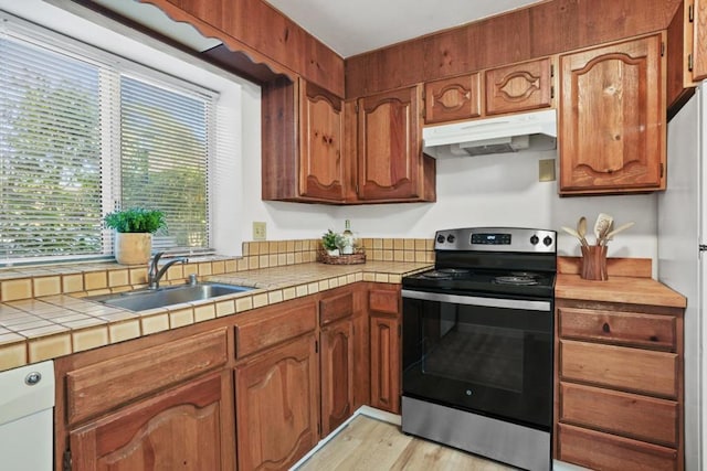 kitchen with sink, stainless steel electric range oven, tile countertops, light wood-type flooring, and fridge