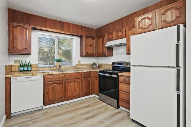 kitchen with sink, tile countertops, white appliances, and light wood-type flooring