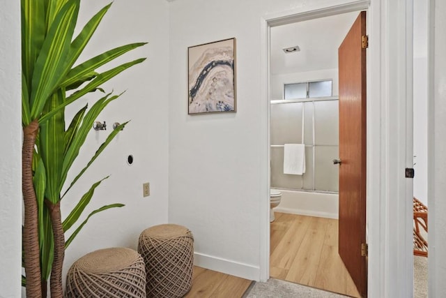 interior space featuring toilet, bath / shower combo with glass door, and hardwood / wood-style floors