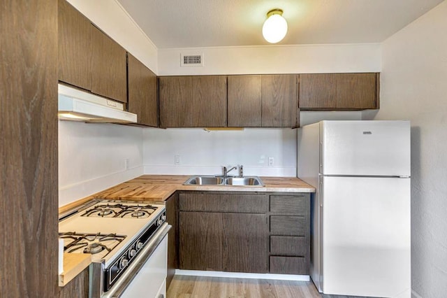 kitchen with sink, white appliances, dark brown cabinets, wood counters, and light wood-type flooring