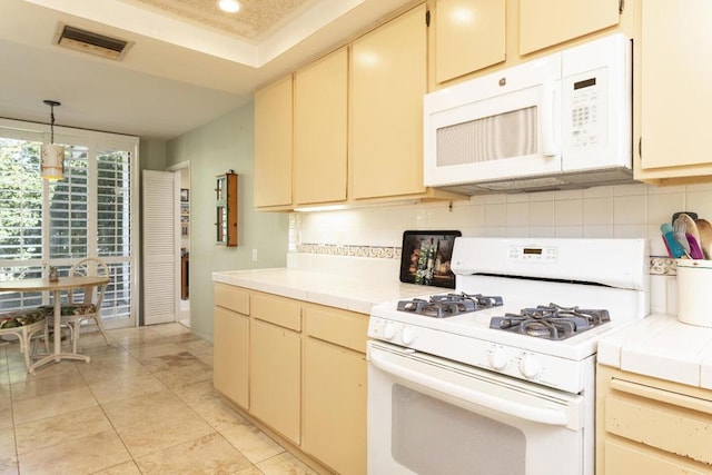 kitchen featuring cream cabinetry, backsplash, white appliances, and hanging light fixtures