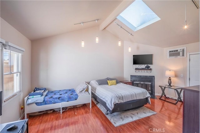 bedroom featuring rail lighting, vaulted ceiling with skylight, hardwood / wood-style flooring, and a wall unit AC