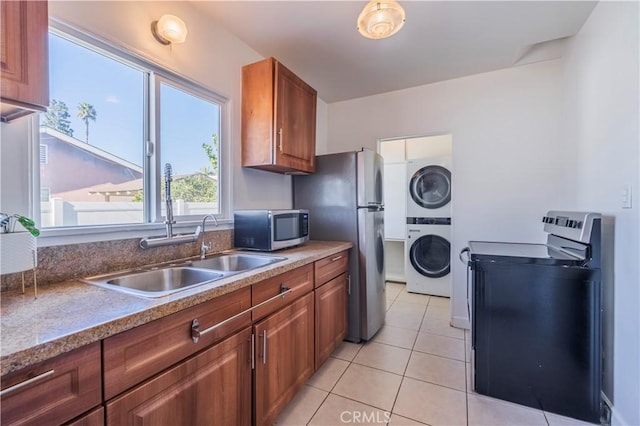 kitchen with light tile patterned floors, appliances with stainless steel finishes, sink, and stacked washer and dryer