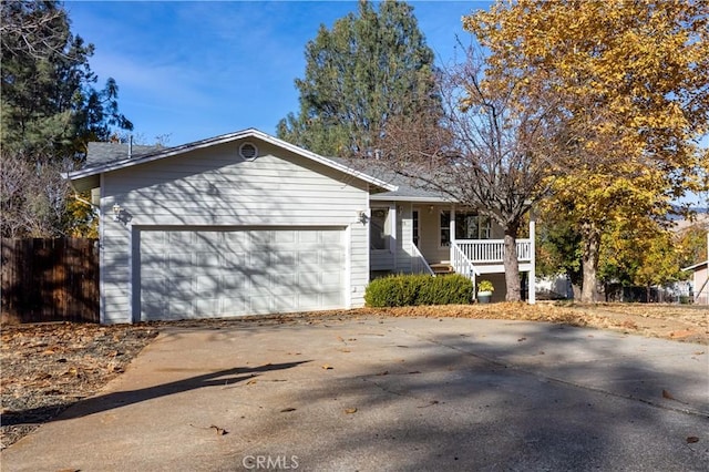 ranch-style house featuring a garage, concrete driveway, covered porch, and fence