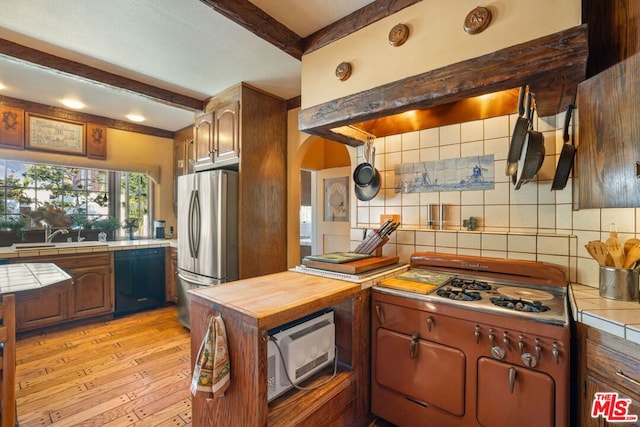 kitchen with sink, light hardwood / wood-style flooring, black dishwasher, tasteful backsplash, and stainless steel refrigerator