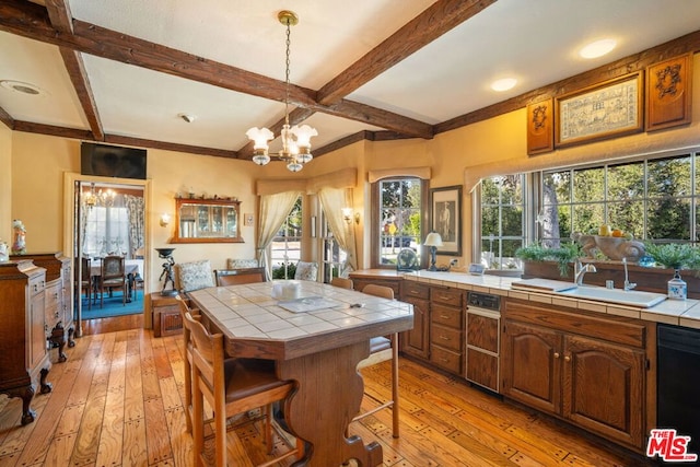 kitchen with beam ceiling, sink, tile counters, a chandelier, and light wood-type flooring