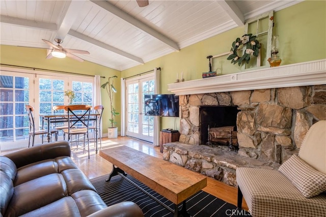 living room featuring ceiling fan, french doors, vaulted ceiling with beams, a stone fireplace, and hardwood / wood-style flooring