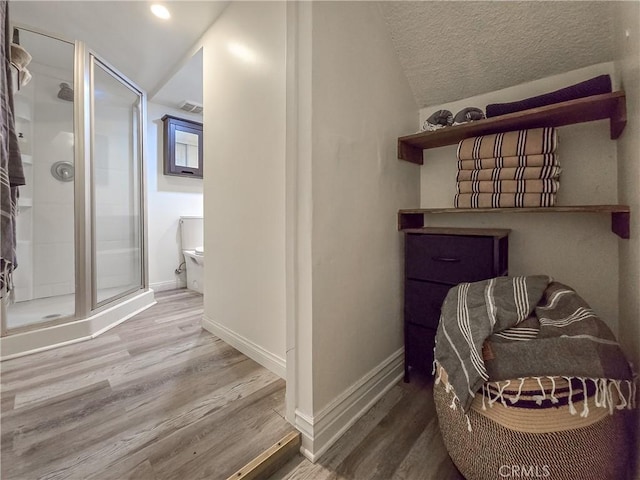 bathroom featuring hardwood / wood-style flooring, toilet, a shower with shower door, and a textured ceiling