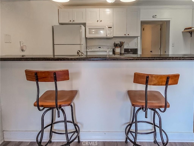 kitchen with a breakfast bar, hardwood / wood-style floors, white cabinets, and white appliances