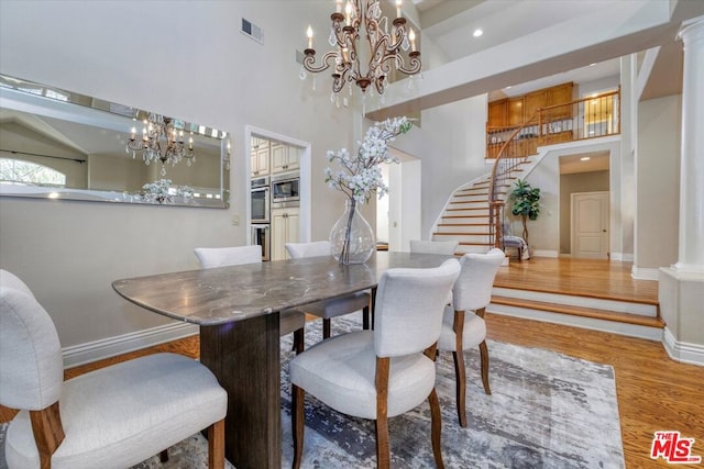 dining area featuring beam ceiling, ornate columns, a notable chandelier, hardwood / wood-style floors, and a towering ceiling