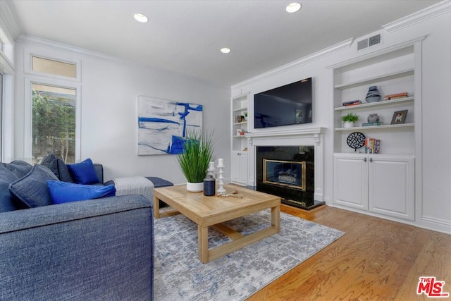 living room featuring a fireplace, light hardwood / wood-style flooring, built in features, and ornamental molding