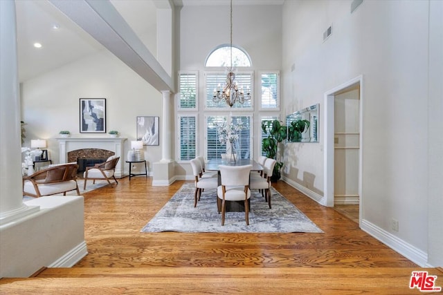 dining area with hardwood / wood-style floors, high vaulted ceiling, an inviting chandelier, a premium fireplace, and decorative columns