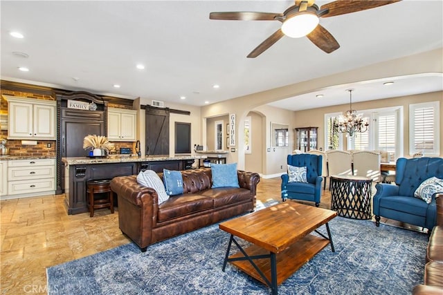 living room with ceiling fan with notable chandelier and a barn door