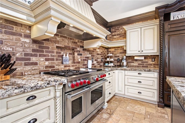 kitchen with light stone countertops, range with two ovens, ornamental molding, and brick wall