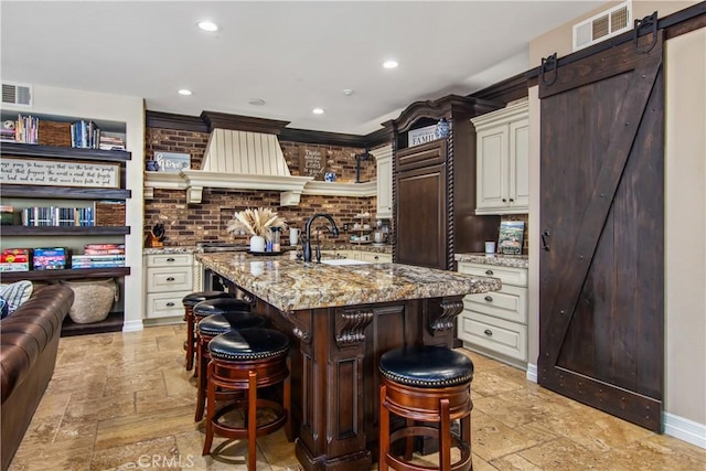 kitchen featuring a breakfast bar area, a barn door, light stone countertops, and a center island with sink