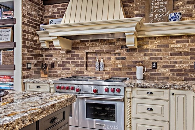 kitchen featuring stone counters, cream cabinets, luxury range, and brick wall