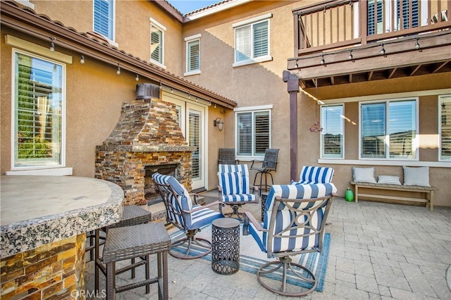 view of patio / terrace with an outdoor stone fireplace and a balcony