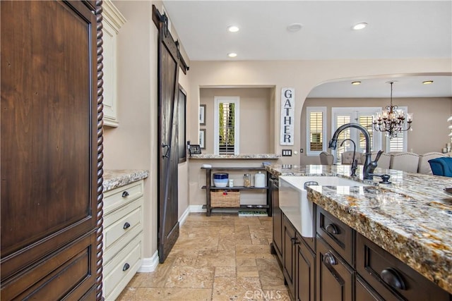 kitchen featuring light stone countertops, sink, a barn door, decorative light fixtures, and a chandelier