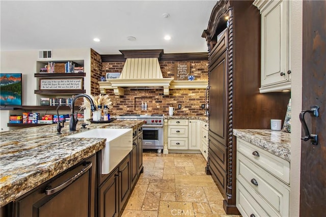 kitchen featuring light stone countertops, sink, premium range, decorative backsplash, and custom exhaust hood