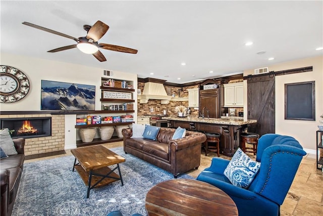 living room with a barn door, ceiling fan, a fireplace, and sink