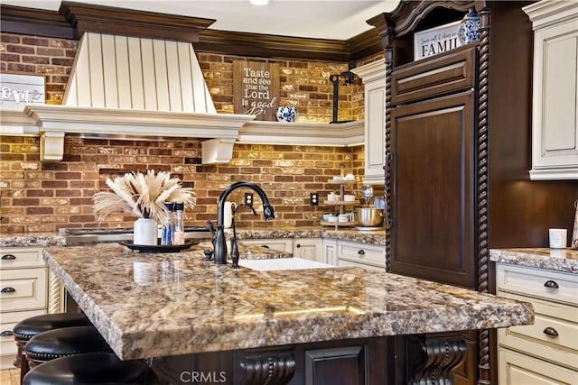 kitchen featuring a center island with sink, light stone counters, and brick wall