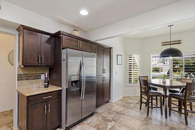 kitchen featuring stainless steel refrigerator with ice dispenser, hanging light fixtures, dark brown cabinetry, and tasteful backsplash