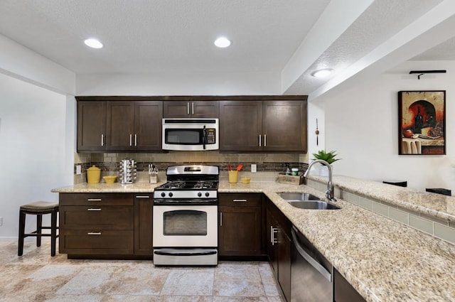 kitchen with light stone counters, sink, stainless steel appliances, and dark brown cabinets