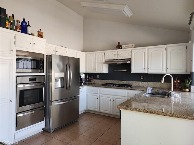 kitchen with appliances with stainless steel finishes, tasteful backsplash, dark stone counters, white cabinets, and sink