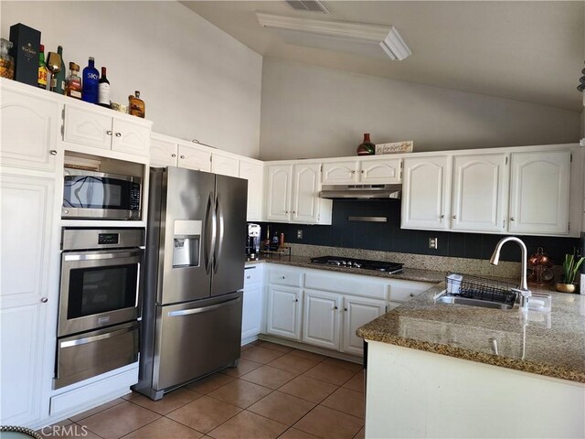 kitchen featuring appliances with stainless steel finishes, tasteful backsplash, dark stone countertops, white cabinets, and sink