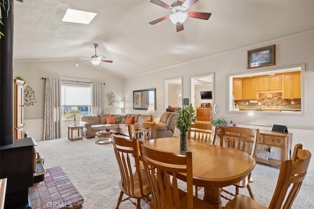 dining area with a wood stove, vaulted ceiling with skylight, ceiling fan, ornamental molding, and carpet floors