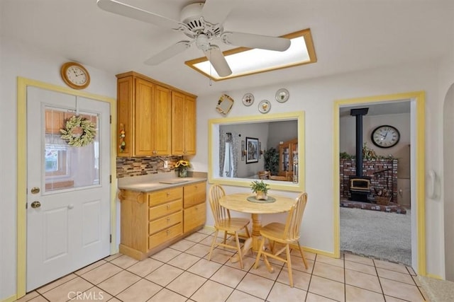 kitchen featuring light brown cabinets, a wood stove, decorative backsplash, ceiling fan, and light tile patterned flooring